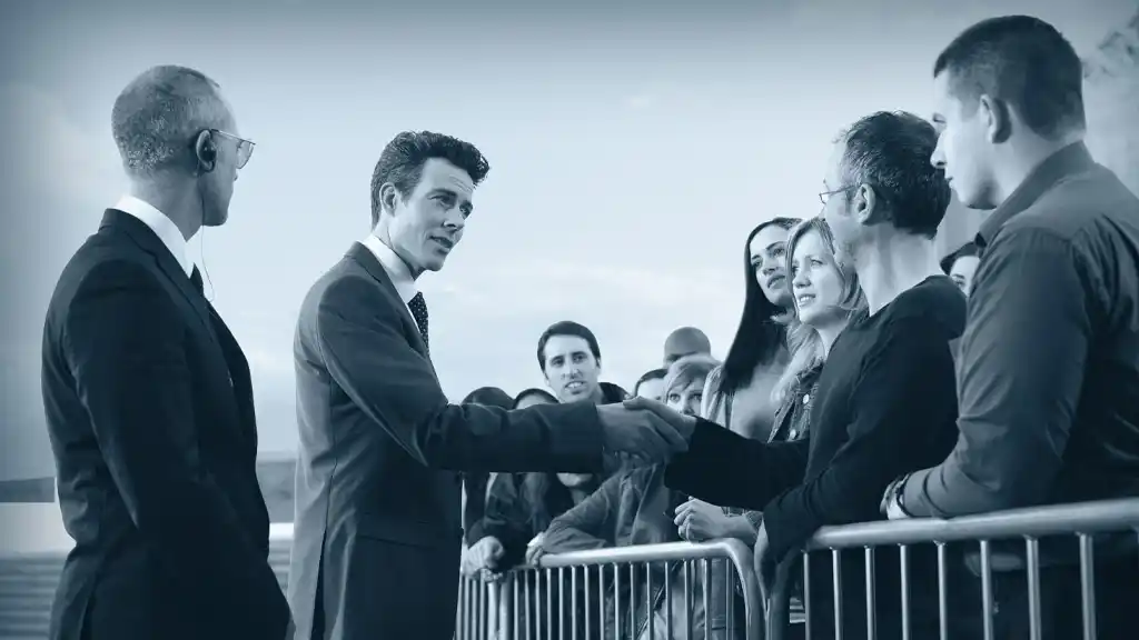 Politician shaking hands with people behind barrier