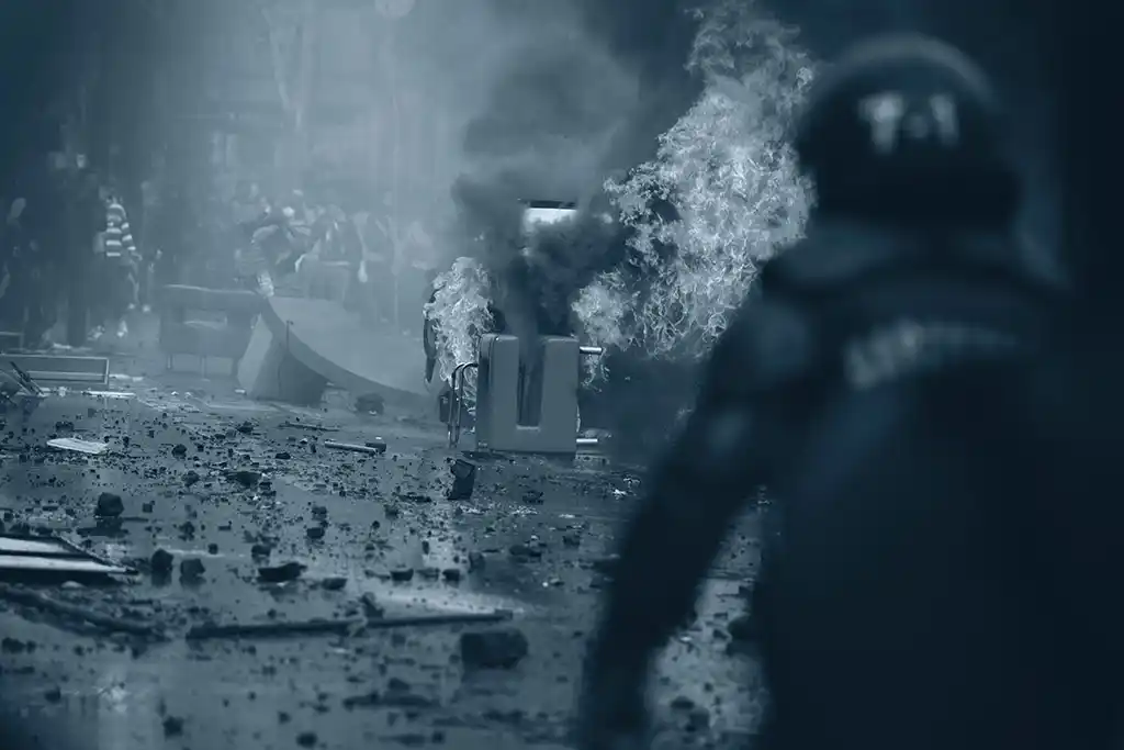 Car on fire with debris on road and male rescue personnel in foreground